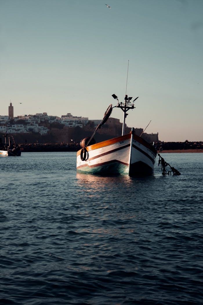 A scenic view of a traditional boat in Rabat harbor during sunset with a historic city backdrop.